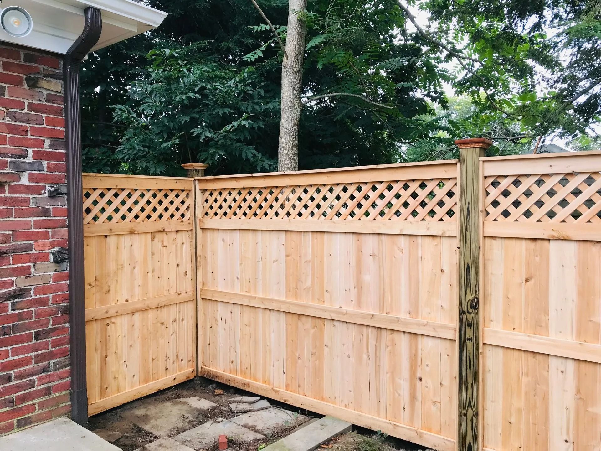 Wooden fence with lattice top section against brick wall and trees.