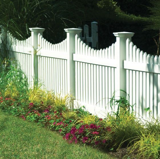 White picket fence with a curved top, bordering a garden with flowers and grass.