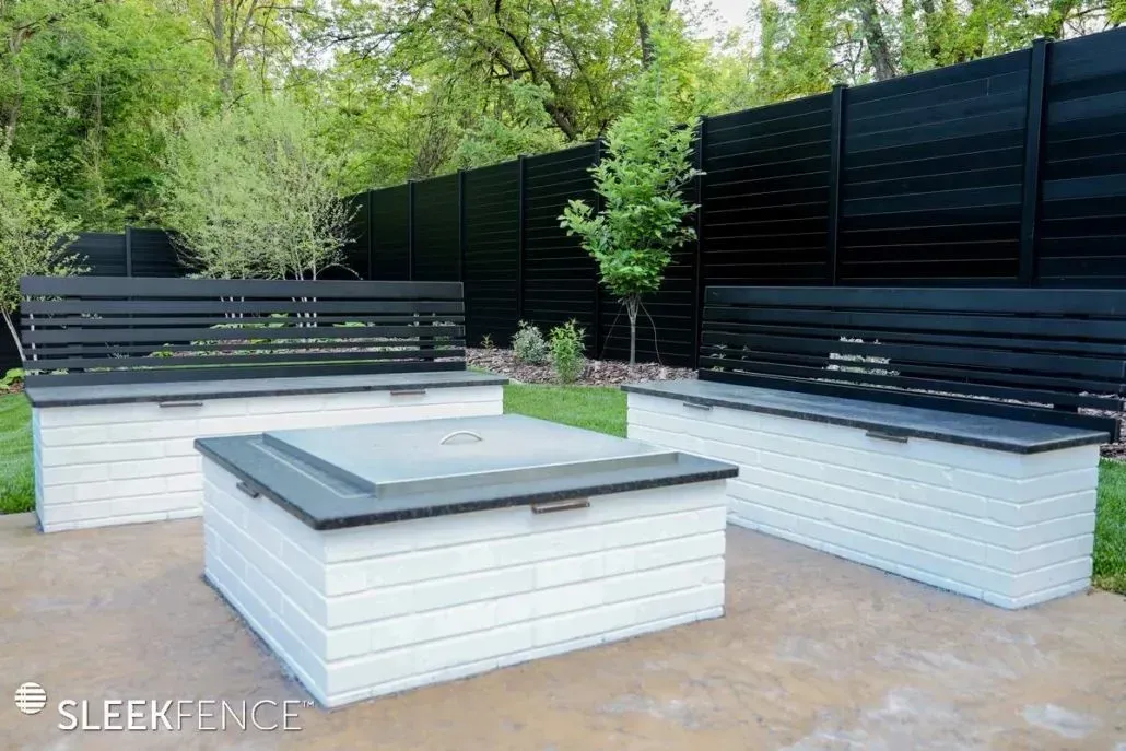 Outdoor seating area with white tables and black benches set against a black fence.