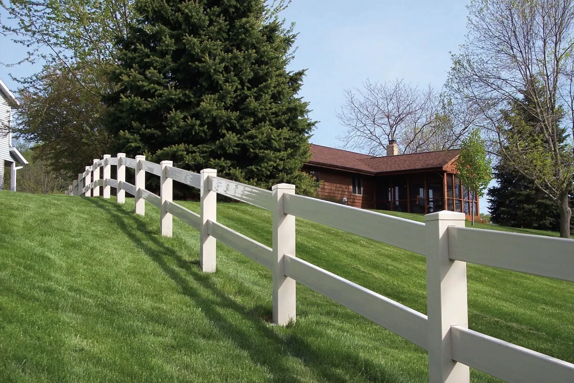 White picket fence in front of a house, surrounded by lush green grass and bushes.