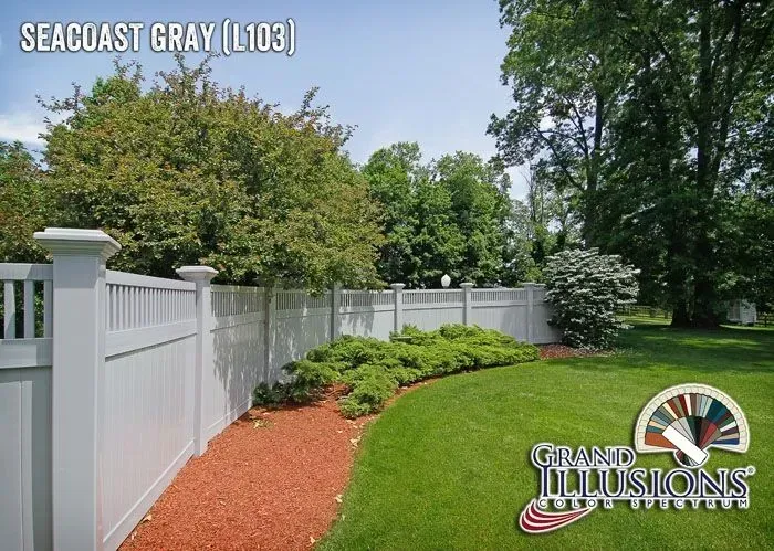 Gray vinyl fence in a grassy yard, with trees and shrubs.