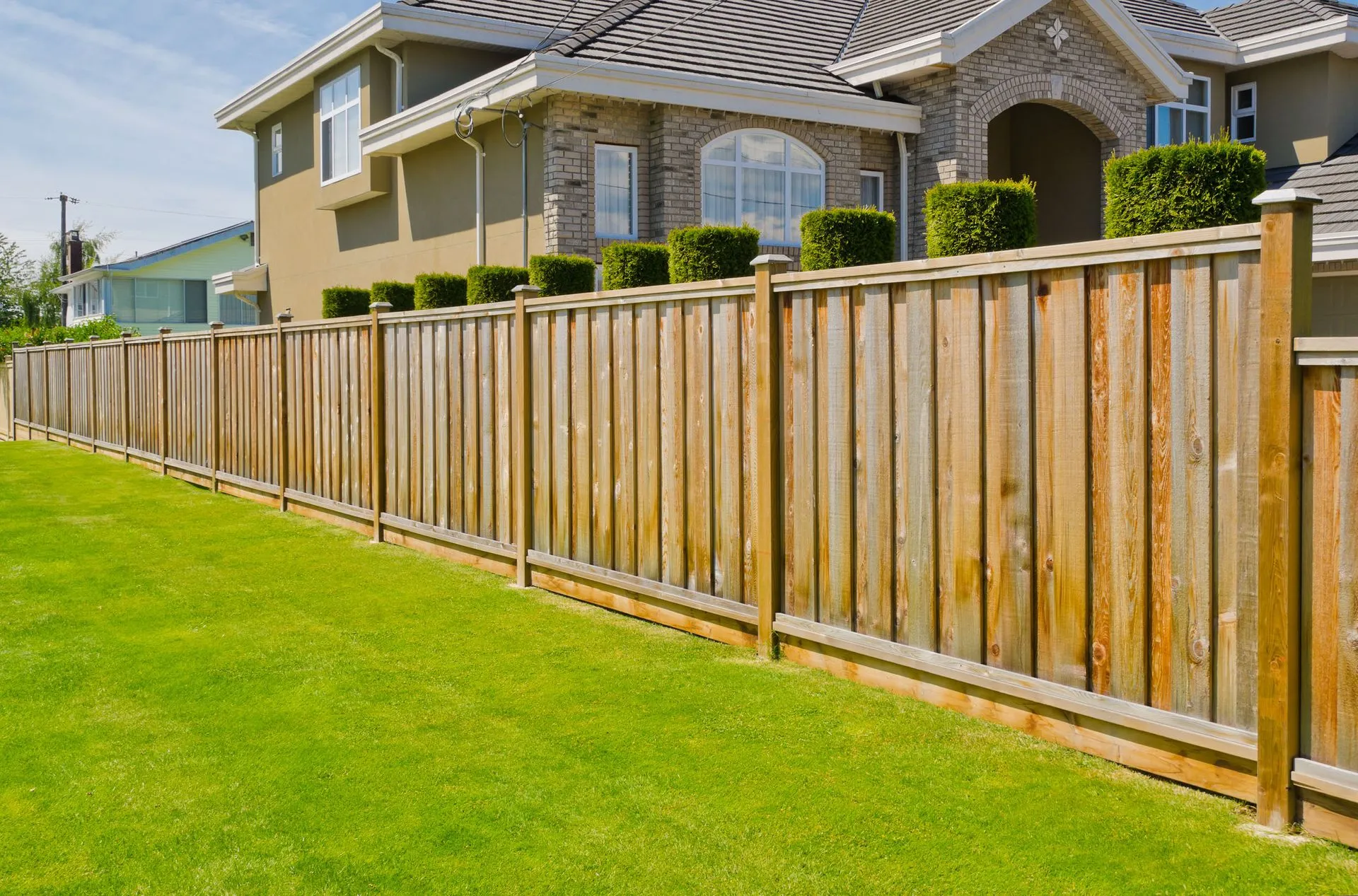 Wooden fence bordering a green lawn in front of a two-story house.